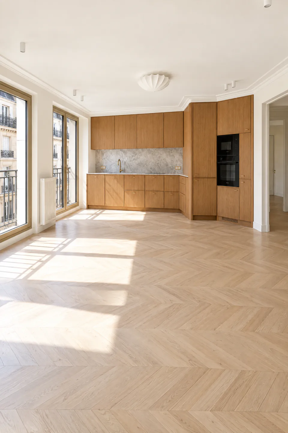 Cuisine ouverte en bois clair sur un séjour au parquet baigné de lumière