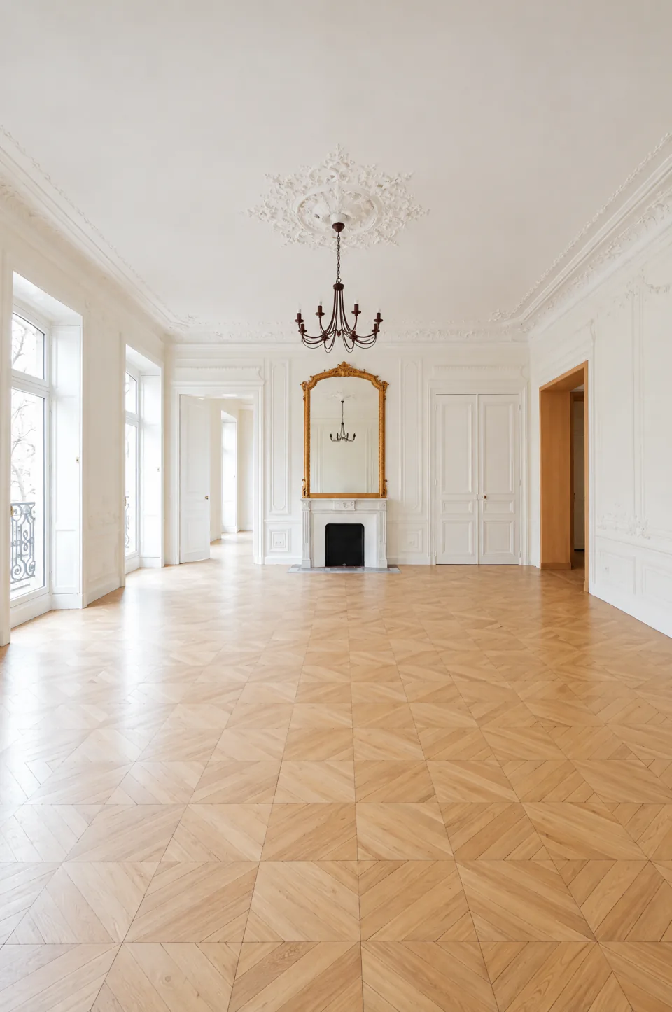 Réception haussmannienne vide avec cheminée, miroir et parquet en point de Hongrie